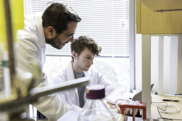 Two men in white lab coats work in a classroom laboratory.